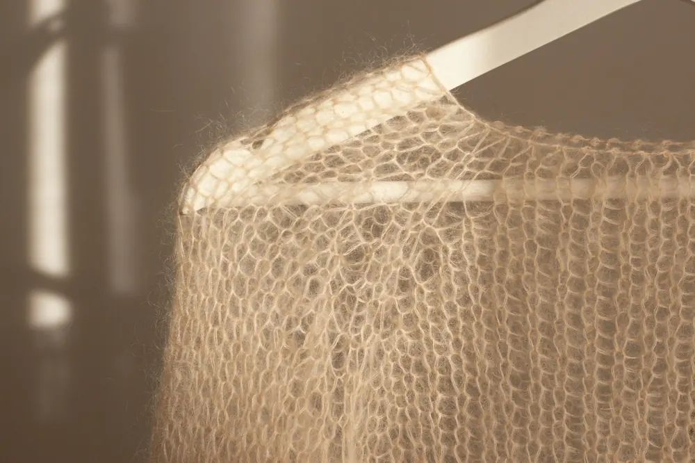 A loose-knit wool jumper on a wooden hanger, backlit by low sun